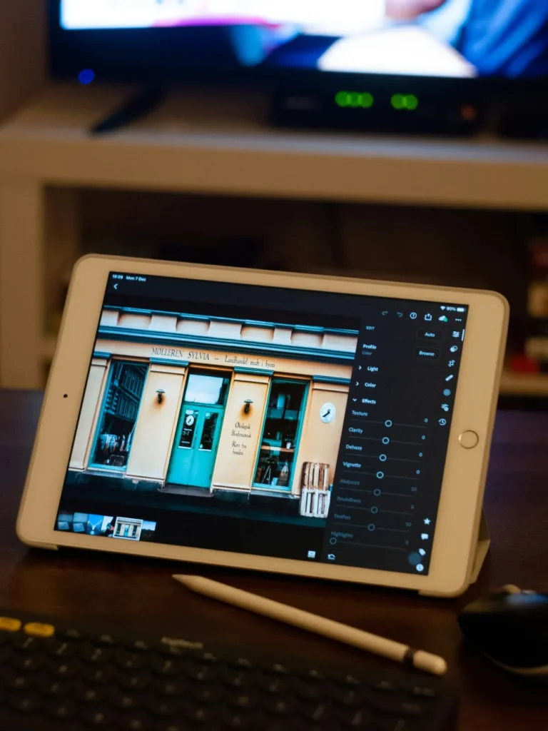 A tablet displaying an image of a storefront, with photo editing tools visible on the side, placed on a desk next to a keyboard and a stylus.